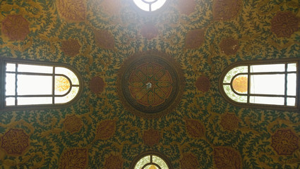 Looking up to a ceiling with oriental ornaments and colorful decorations of a dome with windows on...