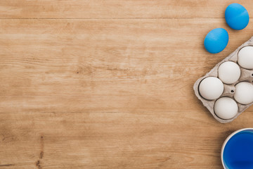 Top view of watercolor blue paint in bowl near chicken eggs and paintbrushes on wooden table