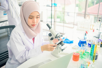 Lab worker. Positive muslim woman looking into the microscope while being at work in the lab