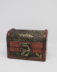 Cofre cerrado de madera decorado con hojas doradas y cierre de latón con fondo blanco.