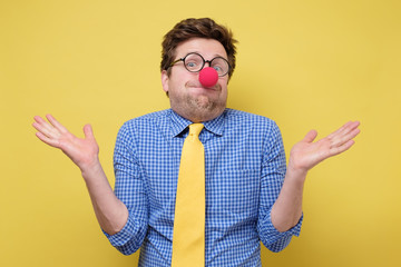 Young funny clown man with red nose and yellow tie showing ignorance