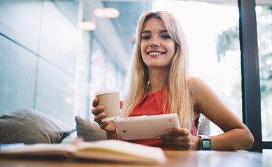 Fototapeta premium Cheerful woman with takeaway beverage and tablet in cafe