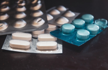 Pills in their package unopened. Tablet strips over one another against dark background.