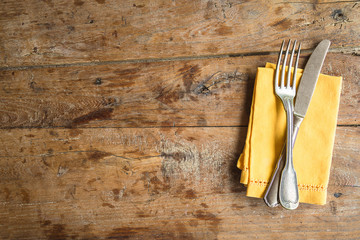 Table setting with antique fork and knife, yellow linen napkin on old wooden background. Space for...