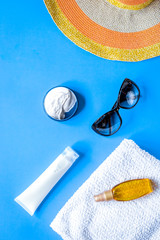Towel, sun lotion, glasses on blue background top view space for text