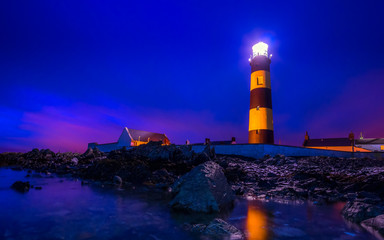 Twilight begins yielding to daylight at St. Johns Point Lighthouse. Rocky coastline with blurred...