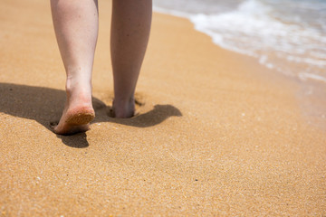 Woman walking barefoot on a beach. Close up leg of young woman walking along wave of sea water and sand on the summer beach. Travel Concept. Woman walking on sand beach leaving footprints in the sand.