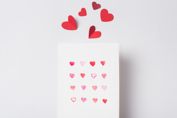 top view of valentines greeting card and paper red hearts on white background