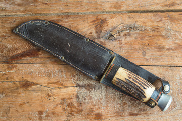 Old hunting knife in leather sheath on old wooden background. Top view