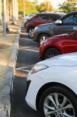 Closeup of front side of white car and other cars parking in outdoor parking lot with natural background in bright sunny day. 