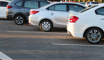 Closeup of rear, back side of white car with  other cars parking in outdoor parking area in bright sunny day..