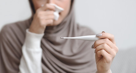 Thermometer in hands of unrecognizable sick muslim woman in hijab