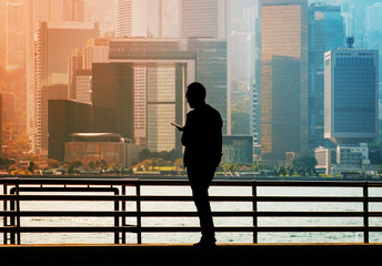 Fototapeta premium Silhouette of a man looking on mobile phone with Hong Kong Island city skyline background