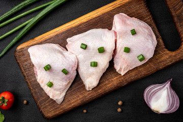 Raw chicken thighs with green onion on black background.