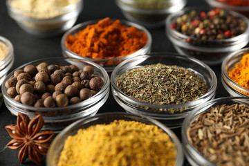 Bowls with different spices and ingredients on black background, close up