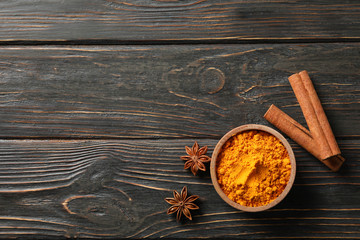 Wood bowl with turmeric and cinnamon on wooden background, top view