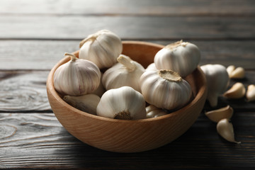Wooden bowl of fresh garlic bulbs, slices on wooden background, top view. Closeup