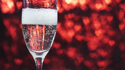 Champagne is poured into a glass on a red background with many hearts, slow motion. Valentine's day concept. - Powered by Adobe