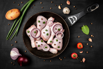 Raw chicken legs with green onion on black background.