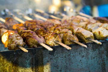 Grilling pork meat on skewers at barbecue party