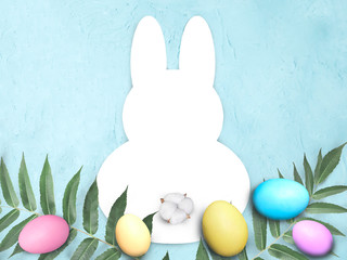 Mock up Easter flat lay with bunny template frame, colored eggs, leaves and cotton flower on blue background. Greeting holiday banner with copyspace.