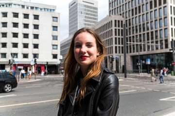 Fototapeta premium Portrait of Young Woman in Leather Coat with Urban Background