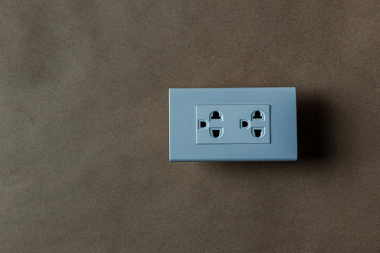 The white electrical plug socket on a brown old wallpaper.