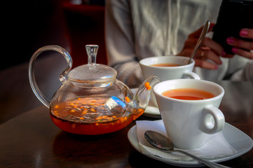 Sea buckthorn tea in glass teapot. Herbal tea is poured into white cups from glass teapot.