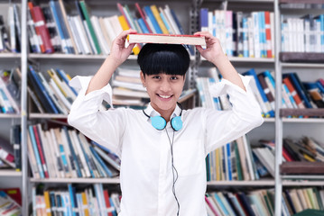 Young teenager put book on her head with happy feeling,searching data from book,at library,blurry...