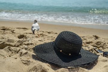 Fototapeta na wymiar Summer holidays relax on the beach abstract background. Women's hat on the beach sand, against the background of the sea and gulls.