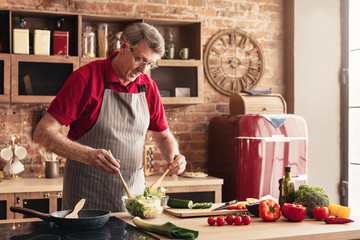 Senior man cooking fresh vegetable salad at kitchen, panorama, free space
