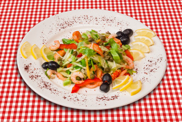 Salad with vegetables, shrimps and black olives decorated with lemon