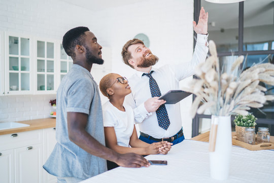 Serious ethnic couple and real estate agent inspecting ceiling in new apartment
