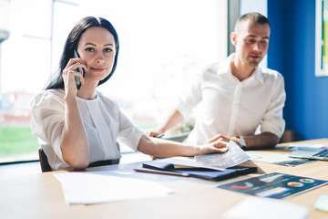 Smiling elegant businesswoman phoning while sitting at table in office