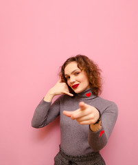 Cheerful hipster cheerful girl shows a hand gesture of the phone and points the index finger to the...