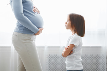 Little girl looking at her expecting mom with reproach