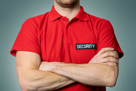 security service guard in red uniform standing on gray background with arms crossed - Powered by Adobe