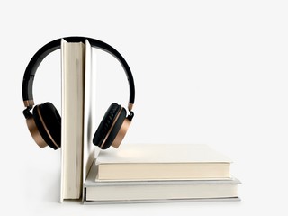Black and golden headphone hanging on a text book. Background with copy space of audio book and E-Learning concept.