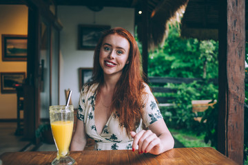 Cheerful redhead woman looking at camera in tropical cafe