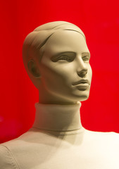 Female mannequin of white color close-up (on the chest) in a sweater on a red background.
