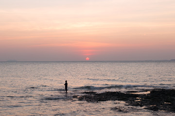 Fototapeta premium Fisherman in the hat on sea pink sunset background.