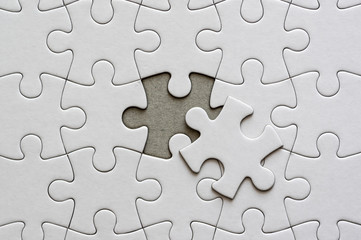 Close up on blank, white jigsaw puzzle pieces. One piece is removed, to the side