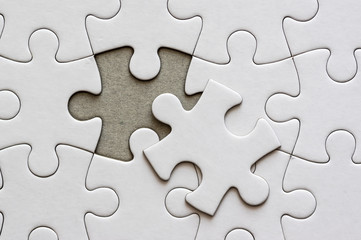 Close up on blank, white jigsaw puzzle pieces. One piece is removed, to the side