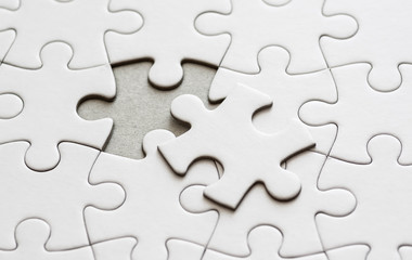 Close up on blank, white jigsaw puzzle pieces. One piece is removed, to the side