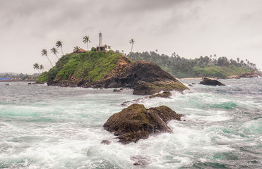 A lighthouse on a high bank is a very good landmark for ships in the stormy waters of the ocean near Sri Lanka