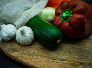 Red pepper, onions, garlic and zucchini in string bag on a wooden board, black background, zero waste concept