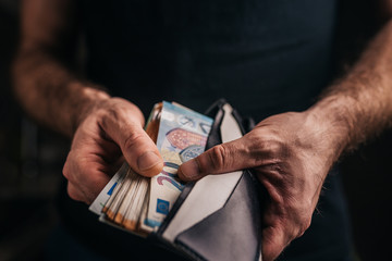 A man puts a stack of euro cash notes in his wallet