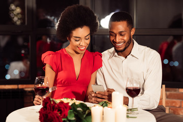 Millennial Afro Couple Using Smartphone During Romantic Date In Restaurant