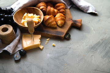 Original tasty French croissants with cheese and grapes on the wooden table. buttery flaky viennoiserie bread roll distinctive crescent shape. Cheese in bowl, knife, cutting board as a background.