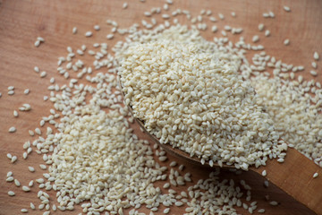 Full spoon of white sesame seed on a wooden board. Wooden spoon on a white background. Home.